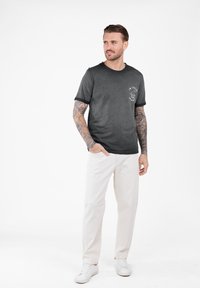 Camiseta de algodón negra con mangas cortas y cuello redondo que presenta una impresión gráfica en el pecho. Se lleva con pantalones blancos y zapatillas.