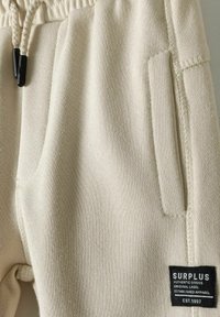 Beige sweatpants met een trekkoord in de taille, textuurstof, zijzakken en een zwart label met witte tekst aan de zoom.
