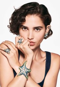 Joyería con temática de estrellas de mar hecha de varias gemas, con diseños intrincados en azul, verde y blanco, llevada en los dedos y la muñeca.