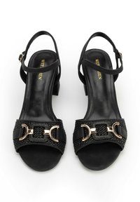 Schwarze Sandalen mit offenen Zehen, niedrigem Blockabsatz, Knöchelriemen, geflochtenen Vorderbändern und dekorativen Schnallen in goldfarbener Metalloptik.