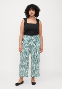 Black sleeveless top with square neckline paired with wide-leg, turquoise and white patterned pants featuring geometric designs and a tie detail.
