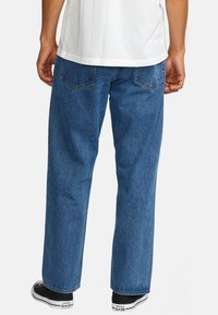Jean en denim bleu avec une coupe ample, jambes droites et poches arrière. Associé à des baskets Converse noires.