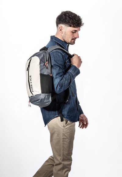 Sac à dos en tissu gris, avec un panneau avant blanc et des accents noirs. Il comporte des fermetures à glissière, des bretelles ajustables et un logo imprimé sur le côté.