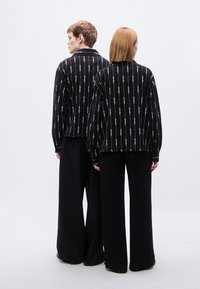 Μαύρα σακάκια με κάθετες λευκές γραμμές, συνδυασμένα με μαύρο παντελόνι φαρδιάς γραμμής. Το ύφασμα φαίνεται μαλακό· απλός γιακάς και σχεδιασμός με άνετη εφαρμογή.