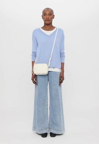 Maglione oversize azzurro chiaro, sotto una maglietta blanche a girocollo, jeans in denim chiaro a gamba larga, piccola borsa a tracolla bianca, scarpe nere.