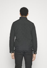 Black quilted jacket with a high collar, snap cuffs, and a tailored fit. Features diagonal stitching and a smooth texture.