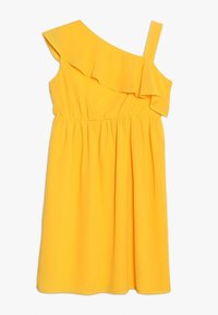 Żółta bezrękawnikowa sukienka z jedną falbanką na ramiączku opadającym z ramienia i elastycznym paskiem w talii, do kolan, na jednolitym białym tle.