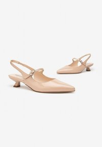 Chaussures slingback en cuir verni beige avec un embout pointu, un petit talon carré et une sangle au niveau de la cheville ornée d'une boucle en métal.