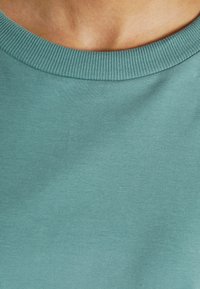 Peça de vestuário azul-turquesa com decote redondo, textura suave e cor sólida, apresentando-se sem padrões ou detalhes de hardware notáveis.