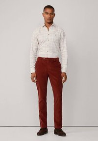 Geruit overhemd met knopen in wit met rode en groene accenten, gecombineerd met bordeauxrode corduroy broek en bruine schoenen. Eenvoudig ontwerp, getailleerde pasvorm.