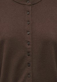 Bruine gebreide cardigan met een ronde halslijn en zes zwarte knopen aan de voorkant. De textuur is zacht en licht geribbeld.