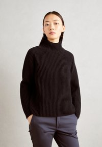 Pulover negru cu guler înalt, cu mâneci lungi, având un model de tricotat texturat. Asortat cu pantaloni bleumarin croiți.
