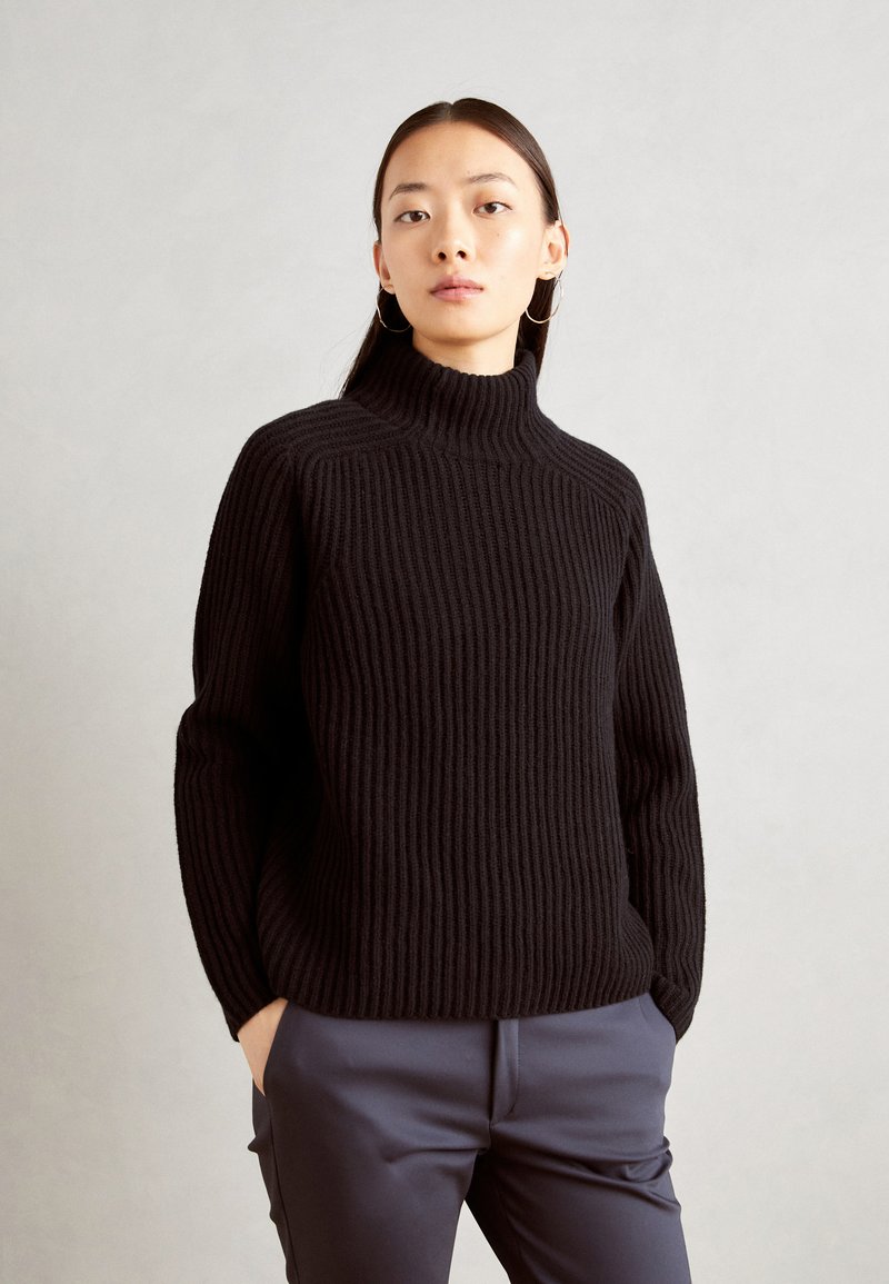 Pulover negru cu guler înalt, cu mâneci lungi, având un model de tricotat texturat. Asortat cu pantaloni bleumarin croiți.