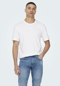 White cotton t-shirt with a crew neckline, relaxed fit, and short sleeves, paired with light blue denim jeans.