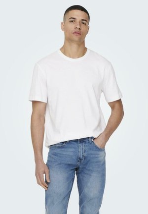 White cotton t-shirt with a crew neckline, relaxed fit, and short sleeves, paired with light blue denim jeans.