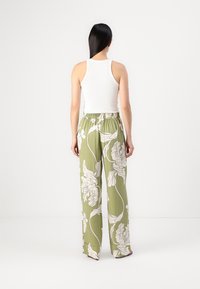 Femme debout de dos portant un haut blanc sans manches et un pantalon large vert olive à imprimé floral blanc.