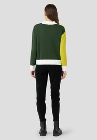 Pull en maille coloré en vert, jaune et blanc avec un col et des poignets côtelés, associé à un pantalon noir texturé et des bottines.