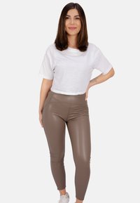 Leggings en simili cuir marron associés à un t-shirt court blanc. Les leggings présentent une texture lisse et un design ajusté, arrivant jusqu'aux chevilles.
