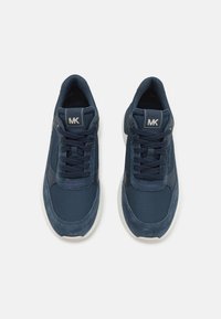 Adidași bleu marin din materiale din plasă și nubuc, vârf rotund, talpă albă groasă, șireturi și logo-ul "MK" pe limbă.