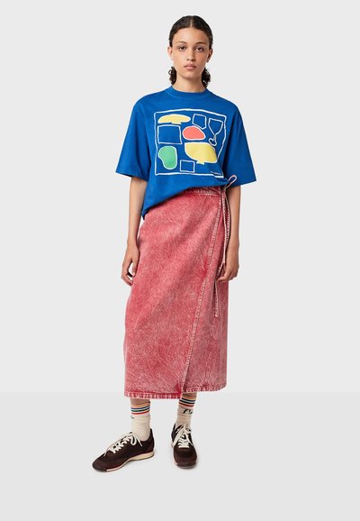 Modrá oversized tričko s barevným geometrickým potiskem; červená džínová zavinovací sukně; pruhované ponožky; tmavé tenisky. Texturovaná tkanina, volný střih.