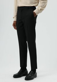 Zwarte op maat gemaakte broek met een smalle pasvorm, platte voorkant, steekzakken aan de zijkant en een gladde textuur, gecombineerd met zwarte loafers en zwarte sokken.