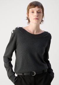 Pull gris foncé avec un large col bateau, des poignets côtelés et des accents décoratifs de boutons argentés sur les épaules. Matière en tricot douce.
