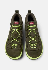 Dwa oliwkowe buty typu high-top z jaskrawozielonymi sznurowadłami i podeszwami, z czerwonym logo "CAMPER" na pięcie.