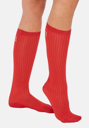 Piros, térdig érő zoknik függőleges bordás mintával és egységes színben. Rugalmas anyag, megerősített szegéllyel a tetején.