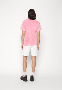Pink tie-dye t-shirt, short sleeves, relaxed fit, paired with white shorts. Black shoes with a chunky sole. Simple design, minimal accents.