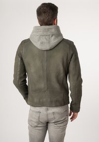 Olivgrüne Lederjacke mit grauem Kapuzen, taillierte Passform, glatte Textur und sichtbare Nähte auf dem Rücken. Auch graue Jeans sind sichtbar.