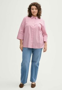 Camicia a righe rossa e bianca con maniche a tre quarti, abbinata a jeans dritti azzurri e scarpe slip-on marroni.