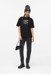 Svart oversized t-skjorte med hvit tekst, svarte rette jeans, svarte kraftige støvler og en liten svart håndveske. Beanie-lue inkludert.