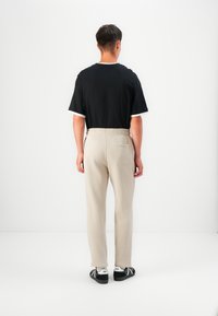 Black short-sleeve shirt with white trim, paired with beige sweatpants featuring an elastic waistband and back pocket, worn with black sneakers.