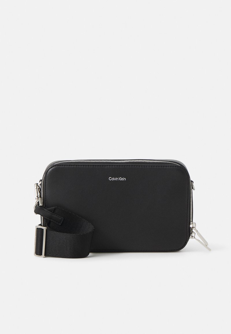 Black zippered clutch from Calvin Klein, featuring a smooth exterior, adjustable strap, and silver-tone hardware. Simple and rectangular design.