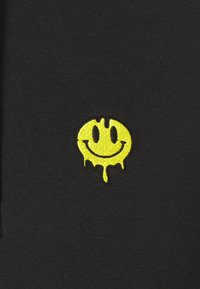 Tessuto nero con un logo sorriso ricamato giallo con gocce nella parte inferiore, posizionato centralmente, con contorni e dettagli ben definiti.