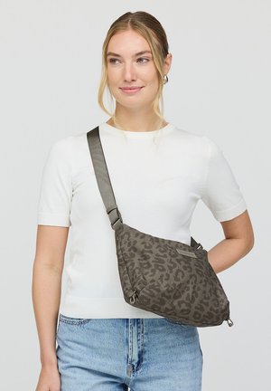 Blonde vrouw die een wit shirt met korte mouwen en een blauwe spijkerbroek draagt, met een grijze crossbodytas met luipaardprint en verstelbare band.
