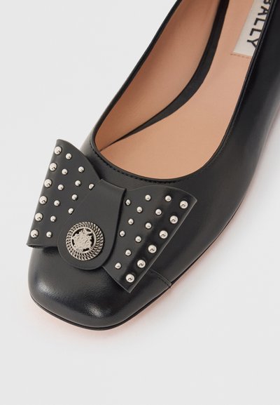 Mocassins ballet en cuir noir avec un bout carré, ornés d'un grand nœud décoré de clous en argent et d'un détail de médaillon circulaire.