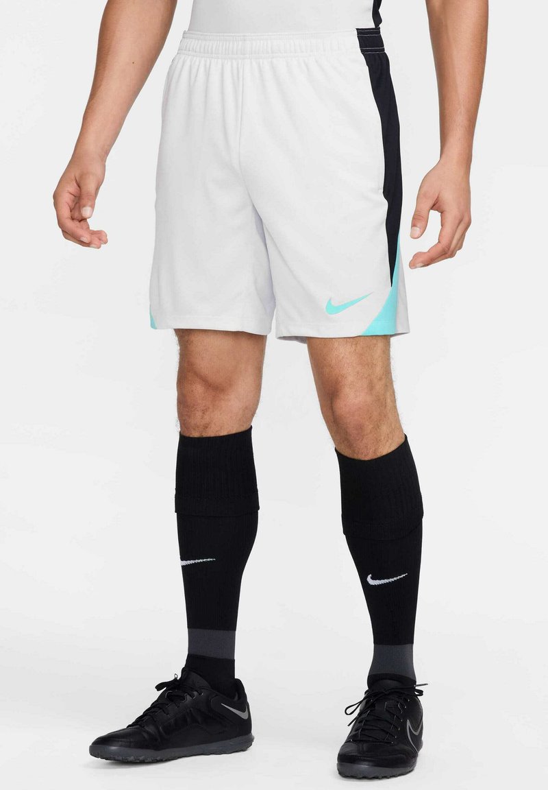 Nike shorts in grijs met zwarte zijpanelen en turquoise accenten; elastische tailleband; gecombineerd met zwarte kniekousen en zwart schoeisel.
