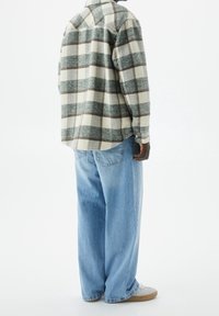 Geruite flanellen blouse in groen en beige, ontspannen pasvorm, gebogen zoom. Lichtblauwe baggy jeans, gedragen met grijze sneakers. Minimalistisch detail.