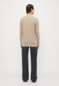 Pull beige avec un col montant, texture côtelée et manches longues, associé à un pantalon large gris foncé avec des ourlets à revers.