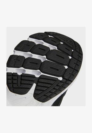 Semelle en caoutchouc texturée noire et blanche d'une chaussure de course avec des rainures profondes et un profil segmenté pour l'adhérence et la flexibilité.