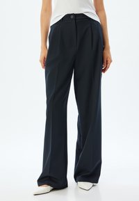 Donkerblauwe wijde broek met voorplooien, een enkele knoopsluiting en zijzakken. Glad materiaal met een gepolijste afwerking.