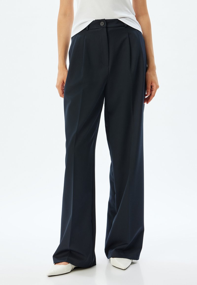 Donkerblauwe wijde broek met voorplooien, een enkele knoopsluiting en zijzakken. Glad materiaal met een gepolijste afwerking.