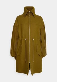 Olivgrön rock med dragkedja, ribbad krage och fransade ärmar. Har två framfickor och justerbara dragskor i midjan.