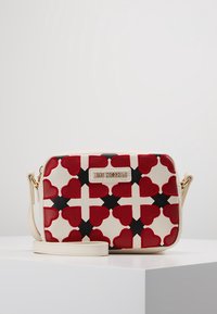 Red and black heart-patterned synthetic bag with a cream base, featuring a logo plaque and a detachable shoulder strap. Rectangular design.