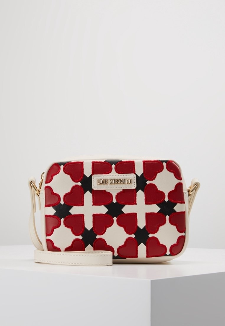 Red and black heart-patterned synthetic bag with a cream base, featuring a logo plaque and a detachable shoulder strap. Rectangular design.