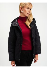 Czarna pikowana kurtka z kapturem, z suwakiem z przodu, bocznymi kieszeniami oraz czerwonym golfem pod spodem, na białym tle.