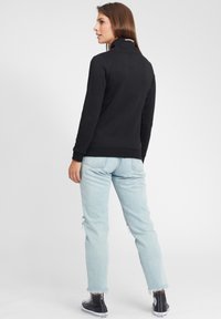 Schwarzer Pullover mit hohem Kragen und gerippten Bündchen, kombiniert mit hellblauen, ausgewaschenen Jeans und schwarzen High-Top-Sneakers.