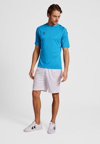 Niebieska koszulka sportowa, krótkie rękawy, okrągły dekolt; zestawiona z białymi szortami. Obuwie białe z czarnymi detalami. Gładki, lekki materiał.