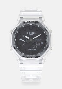 Montre G-Shock avec un boîtier et un bracelet en plastique transparent, cadran noir, aiguilles lumineuses et affichage numérique. Elle comprend des fonctions de chronographe et d'alarme.